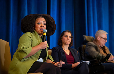 Image of Taryn Williams speaking into a microphone on the AUCD stage next to two other presenters.